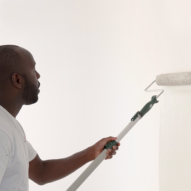 A painting contractor rolling white paint onto a primed wall. A painting contractor rolling white paint onto a primed wall.