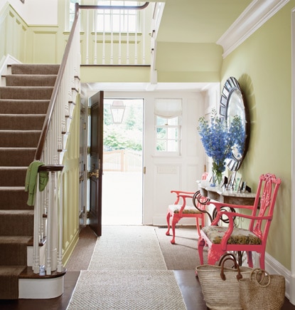 A front door opens into a pale green entryway featuring a console table and two colorful side chairs. A front door opens into a pale green entryway featuring a console table and two colorful side chairs.