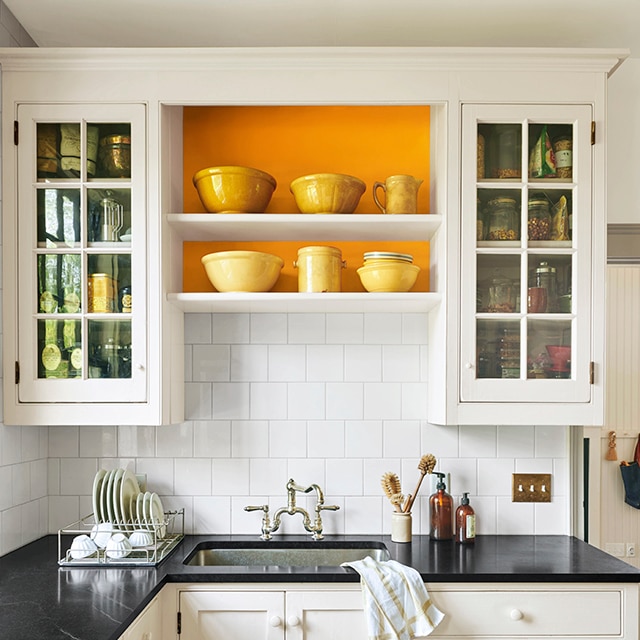 Cuisine blanche au comptoir noir avec mur d’accent orange derrière des étagères suspendues Cuisine blanche au comptoir noir avec mur d’accent orange derrière des étagères suspendues