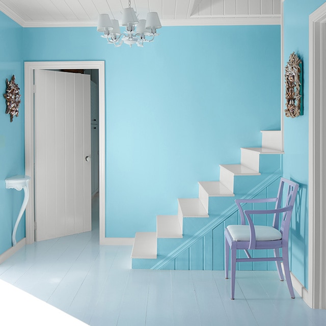 A sunlit home entryway with turquoise blue painted walls, a white shiplap ceiling and doors, white trim, and a fun turquoise blue and white painted staircase. A sunlit home entryway with turquoise blue painted walls, a white shiplap ceiling and doors, white trim, and a fun turquoise blue and white painted staircase.