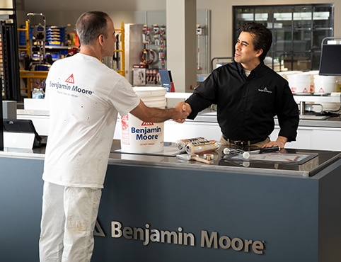 Un détaillant derrière un comptoir Benjamin Moore aide un entrepreneur à acheter de la peinture. Un détaillant derrière un comptoir Benjamin Moore aide un entrepreneur à acheter de la peinture.