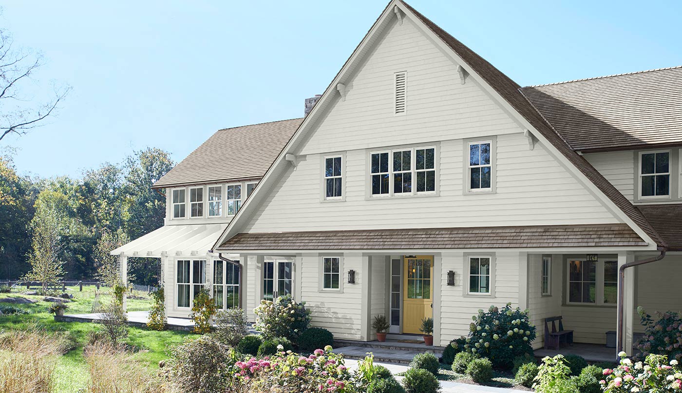 A white-painted house with a yellow door, and green bushes and grass in front.