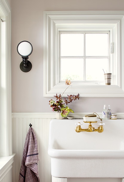 Un lavabo blanc surdimensionné devant un mur lavande pâle orné de lambris blancs. Un lavabo blanc surdimensionné devant un mur lavande pâle orné de lambris blancs.