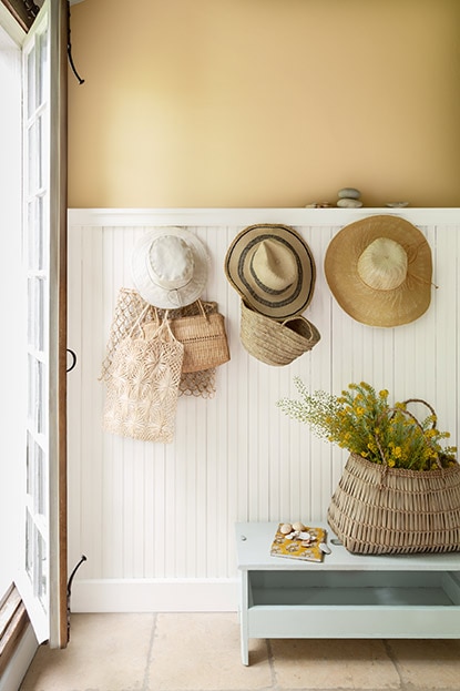 Trois chapeaux et des sacs sont accrochés sur les lambris de bois blancs recouvrant les trois quarts de la hauteur d’un mur beige doré. Trois chapeaux et des sacs sont accrochés sur les lambris de bois blancs recouvrant les trois quarts de la hauteur d’un mur beige doré.