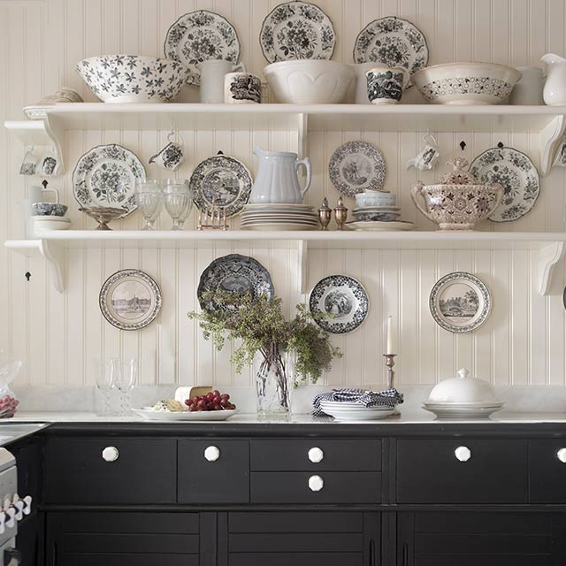 Une cuisine de style campagne française peinte en blanc présentant des étagères ouvertes et des assiettes à motifs au-dessus d’armoires peinturées en noir, et un plancher en carrelage noir et blanc. Une cuisine de style campagne française peinte en blanc présentant des étagères ouvertes et des assiettes à motifs au-dessus d’armoires peinturées en noir, et un plancher en carrelage noir et blanc.