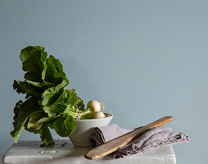 Feuilles vertes dans un petit bol sur une table avec du linge de maison et un ustensile en bois devant un mur peint en bleu. Feuilles vertes dans un petit bol sur une table avec du linge de maison et un ustensile en bois devant un mur peint en bleu.