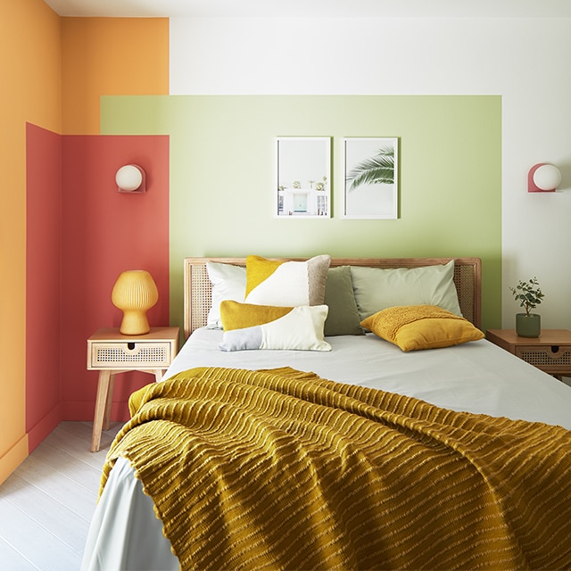 A small, contemporary bedroom with a painted color block wall design in green, red and orange against white-painted walls, and a double bed with an orange throw. A small, contemporary bedroom with a painted color block wall design in green, red and orange against white-painted walls, and a double bed with an orange throw.