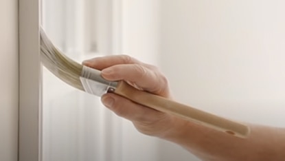 A person brushing white paint onto trim. A person brushing white paint onto trim.